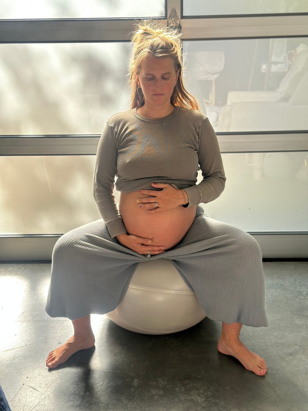 Pregnant woman seated wide on a birth ball, hands on her belly, breathing