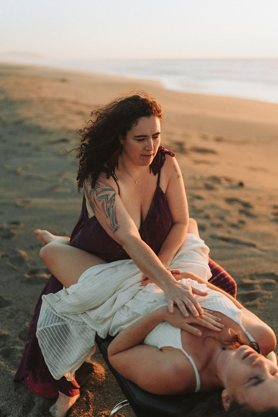 Dr. Tara Morrison offering hands-on care to a woman on the beach at golden hour